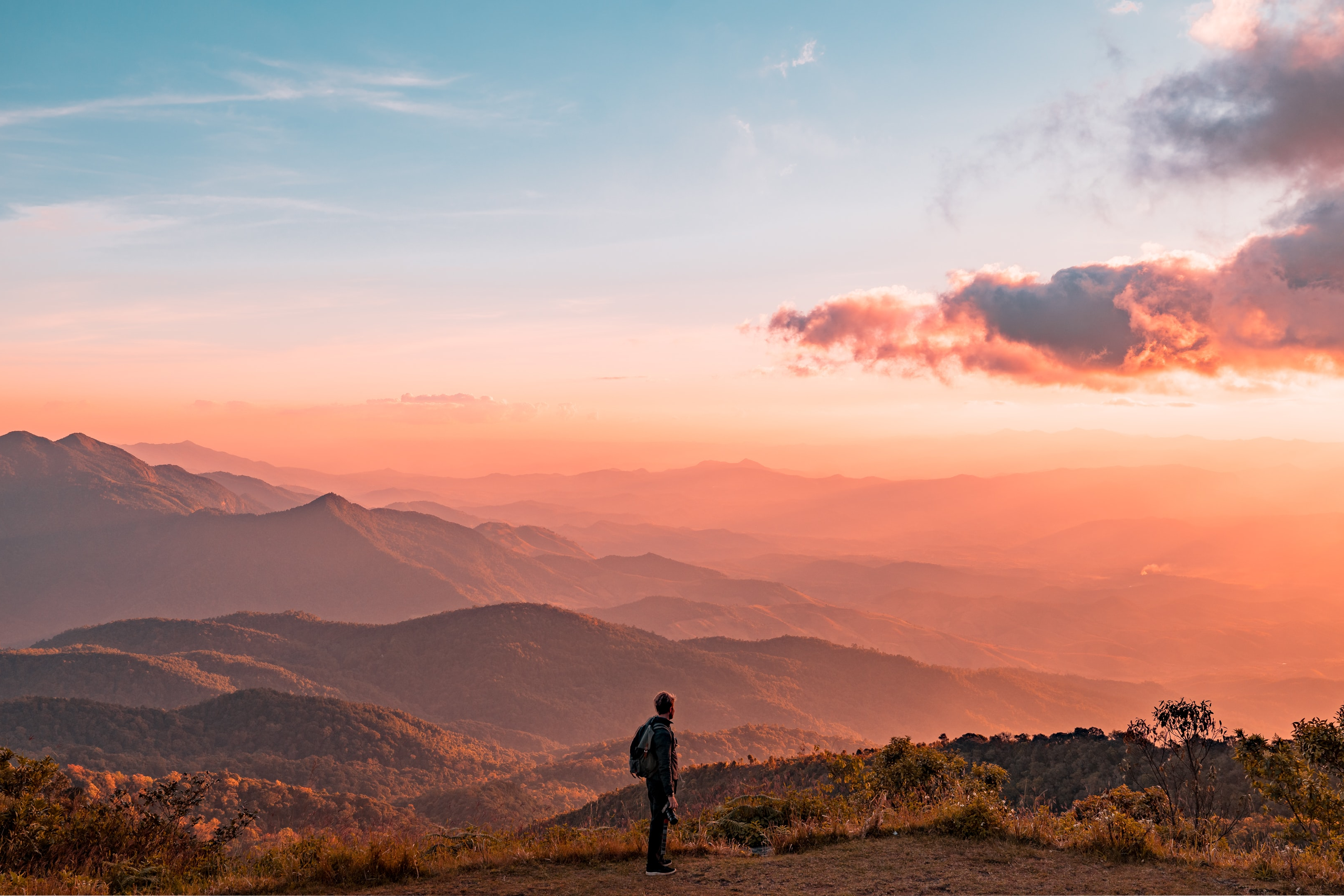Man with backpack overlooking a peaceful mountainside at sunset